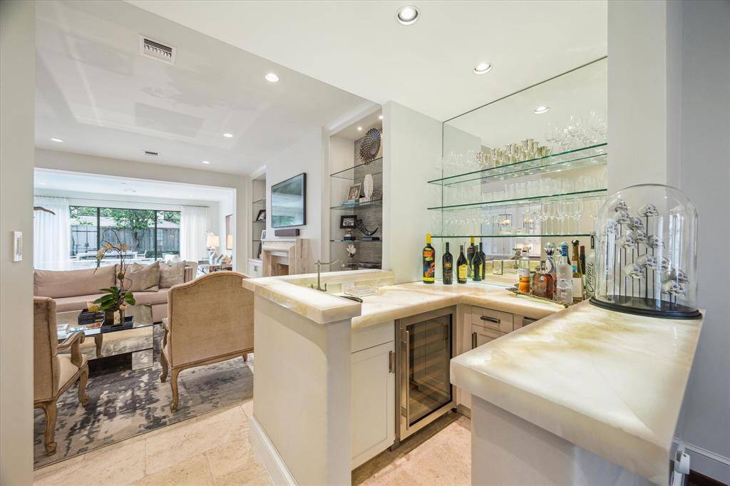 Located between the Living Room and the Family Room is the WET BAR  with its travertine tile flooring, onyx countertop with built-in lighting, glass shelving, mirrored backsplash, metal sink, leather wall accent, stainless Scotsman ice maker and stainless Sub-Zero wine chiller.