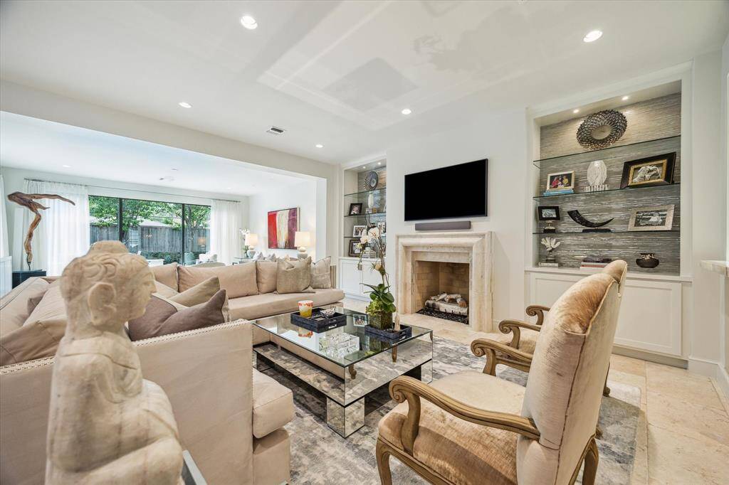 View from the Living Room looking toward the spacious FAMILY ROOM (22 X 18) with its travertine tile flooring, gaslog fireplace with stone surround flanked by built-in cabinets with glass shelving/designer wallpaper, ceiling speakers, recessed/art lighting and base molding.