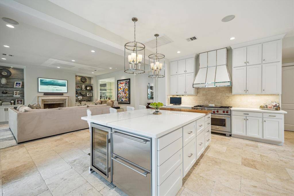 View of the Kitchen showing the stainless appliance package (side by side Sub-Zero refrigerator/freezer, Wolf dual ovens, Wolf warming drawer, Wolf 4 burner gas range/griddle, Sharp microwave, Samsung dishwasher, 2 Sub-Zero refrigerated beverage drawers, Sub-Zero wine chiller), appliance garage, porcelain farmhouse sink, under cabinet lighting, travertine tile flooring, marble counters with travertine tile backsplash, faucet with pull-down feature, recessed/art lighting, walk-in pantry with utility closet.