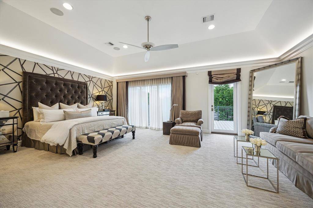 The elegant PRIMARY SUITE (23 X 17) features carpeted flooring, raised ceiling with cove lighting, 3-panel windows with designer sheers/blackout shades, papered accent wall, hidden flush-wall storage closet, ceiling fan with light, ceiling speakers, recessed lighting, crown/base molding, glass door to Balcony (13 X 10) with railing/two gas lanters, En Suite Bath.