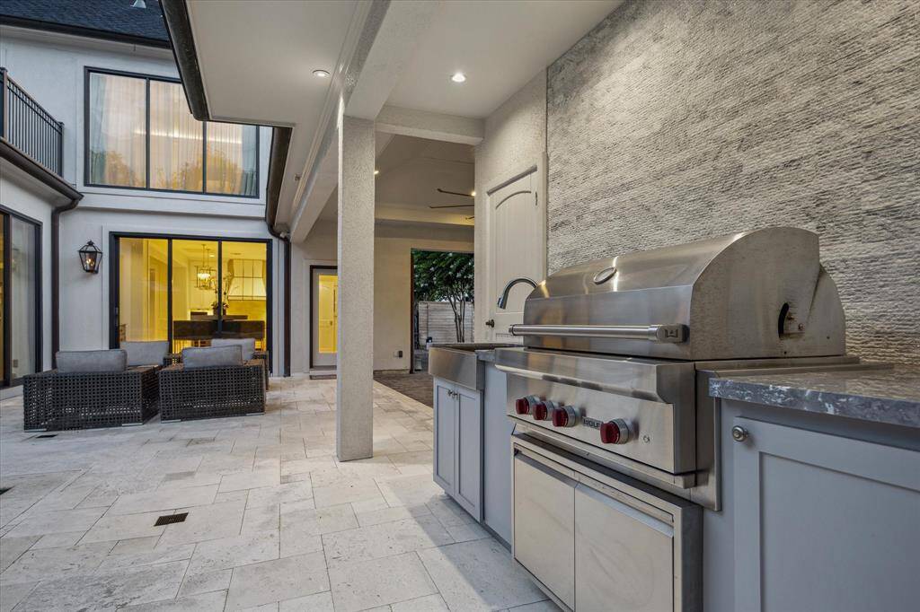 View of the covered SUMMER KITCHEN with its marble countertop, stainless sink, Wolf gas grill, etched stone wall accent, speakers, TV niche and gaslog fireplace.