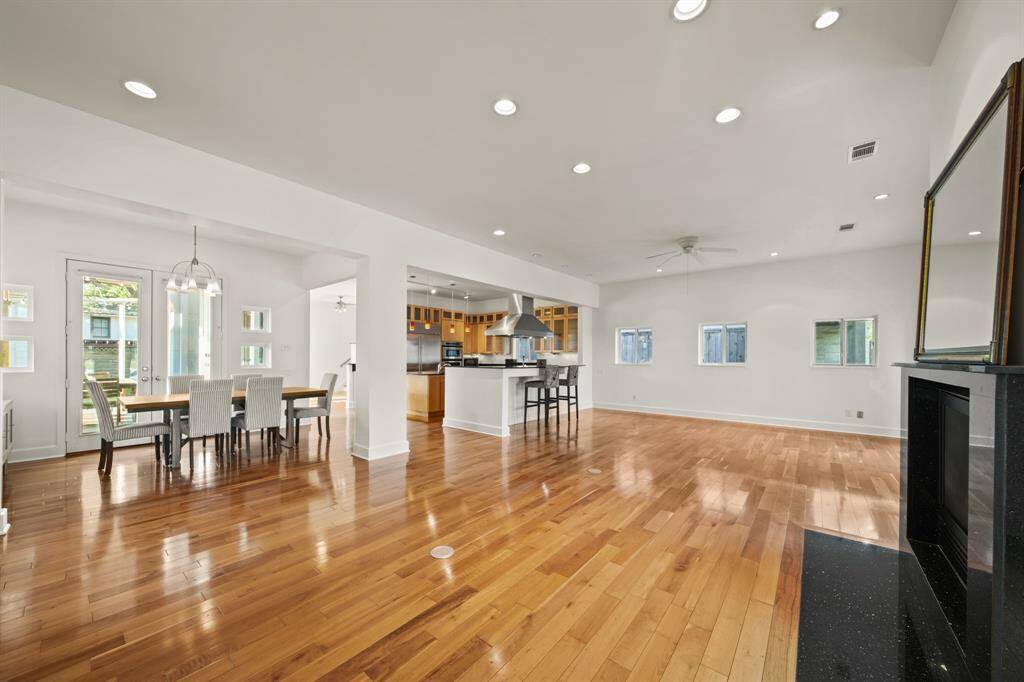 View of living room, kitchen and dining, with fireplace, wood floors, natural sunlight and recessed lighting.