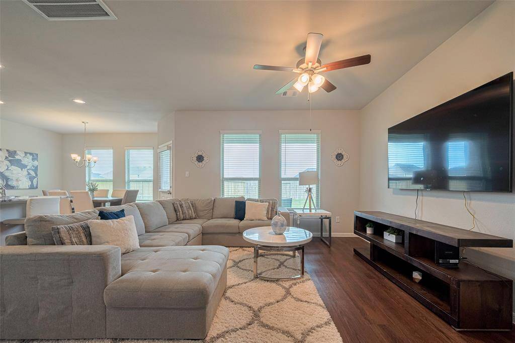 A welcoming living area anchored by warm wood-look flooring and bathed in natural light from tall windows that stretch nearly floor-to-ceiling, creating an uplifting ambiance throughout the day.