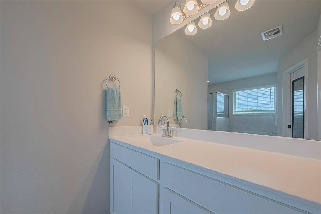 A wide, well-lit mirror sits above a pristine white vanity with ample cabinetry, making everyday routines feel elevated.