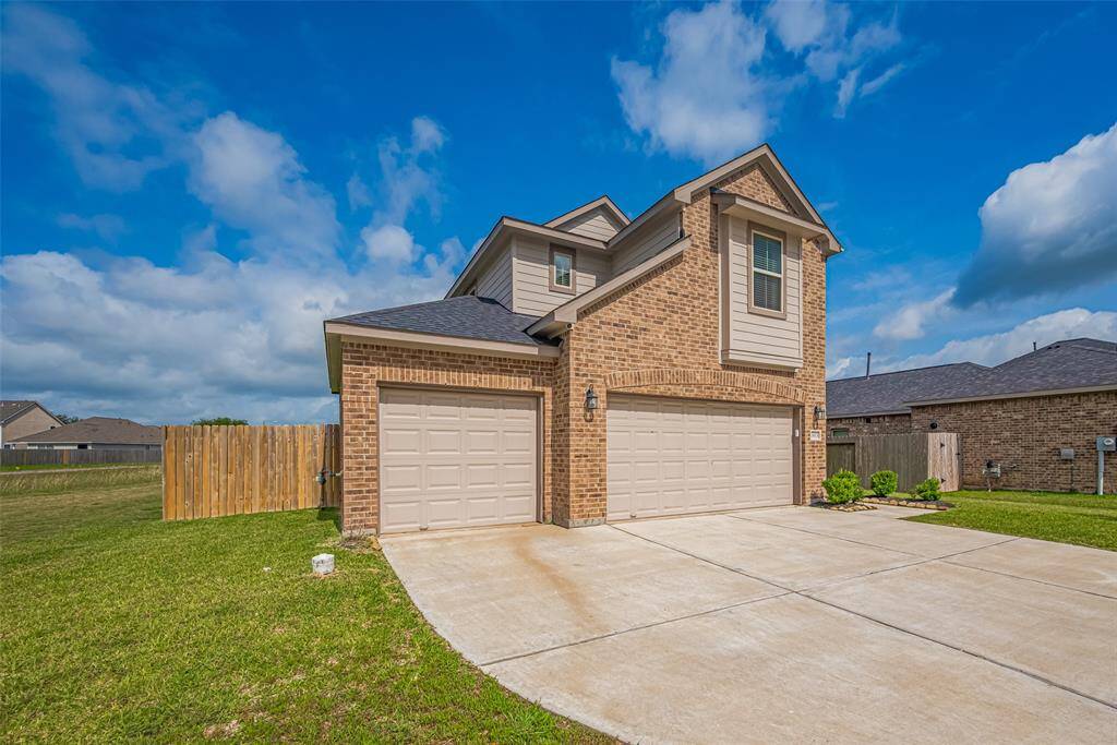 he home glows in natural daylight, showcasing its three-car garage, manicured lawn, and spacious concrete driveway.