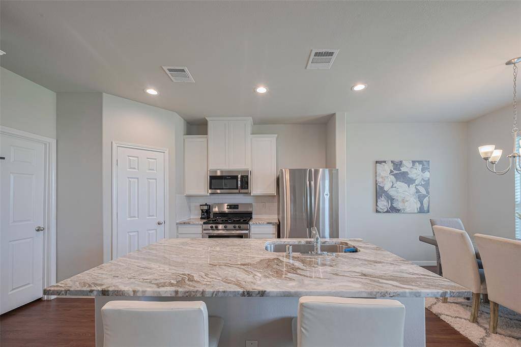 The kitchen island offers bar seating and an undermount sink, glowing beneath soft recessed lighting that enhances its granite surface.