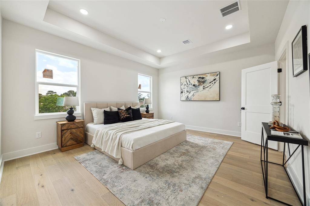Experience serene comfort in this spacious primary bedroom, featuring abundant natural light, elegant tray ceilings, and stylish decor. Perfect for relaxation and rejuvenation.