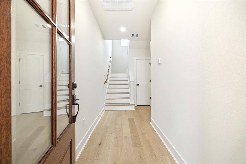 Step into a bright and welcoming entrance, featuring elegant wood flooring and a modern, open staircase leading to your new home.