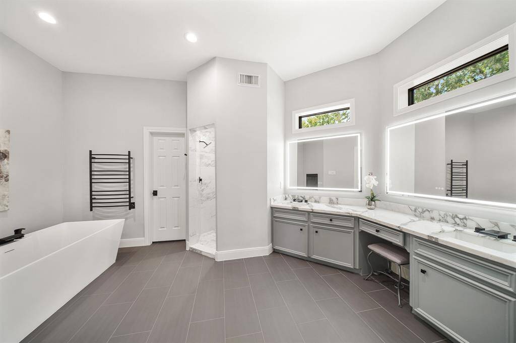 This spa-like Primary Bath is grand in size and functionality. The space boasts marble countertops, a pair of undermount sinks adorned with waterfall style faucets, a central makeup vanity, and desirable LED lit mirrors. The cased transom windows above allow natural light to fill the space without compromising on privacy.
