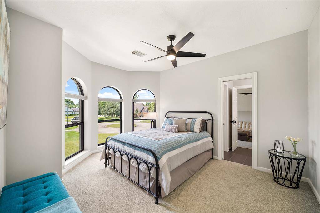 This Secondary Bedroom boasts plush carpeting, a walk-in closet, 5-blade ceiling fan, and ensuite Bathroom. The trio of windows, with arched transoms above, overlook the Front Yard.