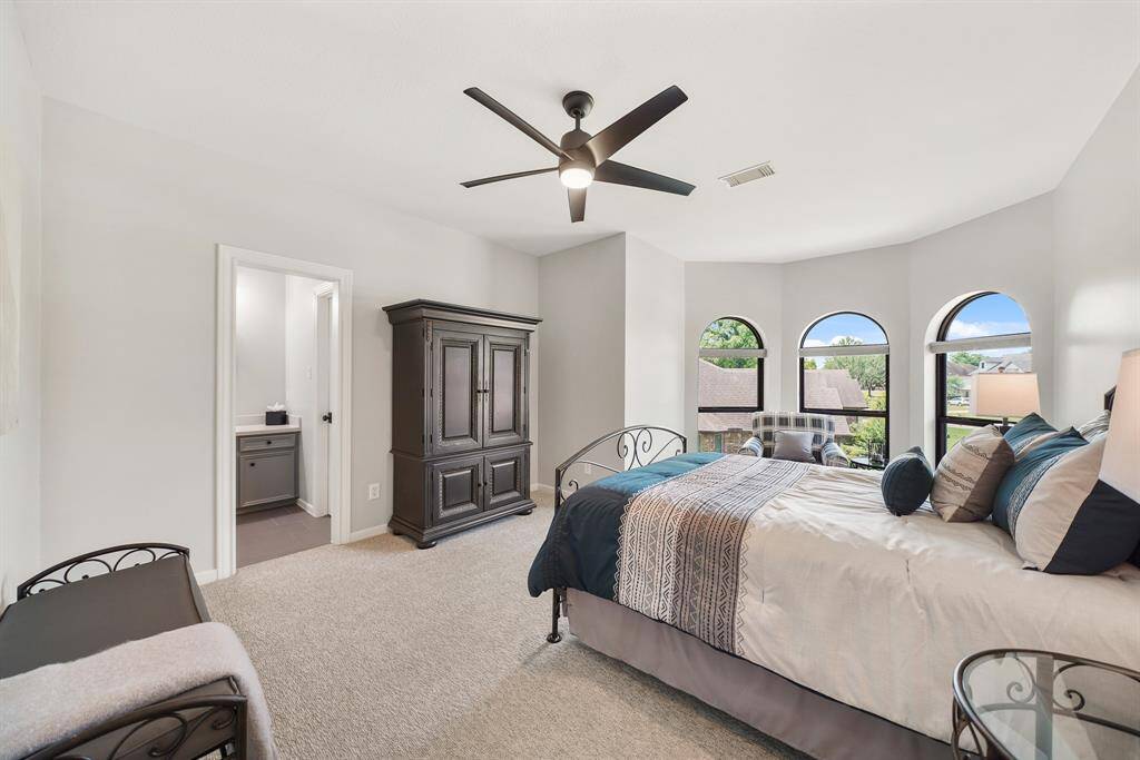 This Secondary Bedroom boasts plush carpeting, a 5-blade ceiling fan, walk-in closet, and a trio of windows with arched transoms above. The space has direct access to a Jack and Jill Bathroom shared with the next Secondary Bedroom.