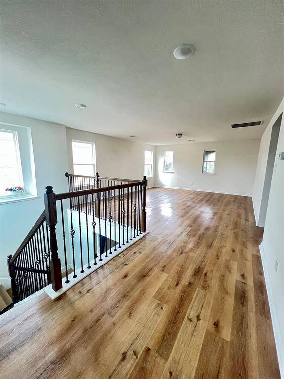 This spacious gameroom room features beautiful wood flooring and multiple windows for natural light. The elegant staircase with wrought iron railings adds a stylish touch. Ideal for a versatile living area or entertainment space.