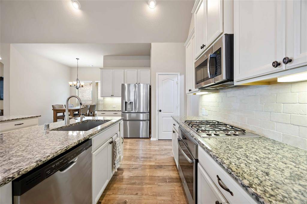 This kitchen is equipped with stainless steel appliances, paired with a white basksplash and a gorgeous granite countertops.