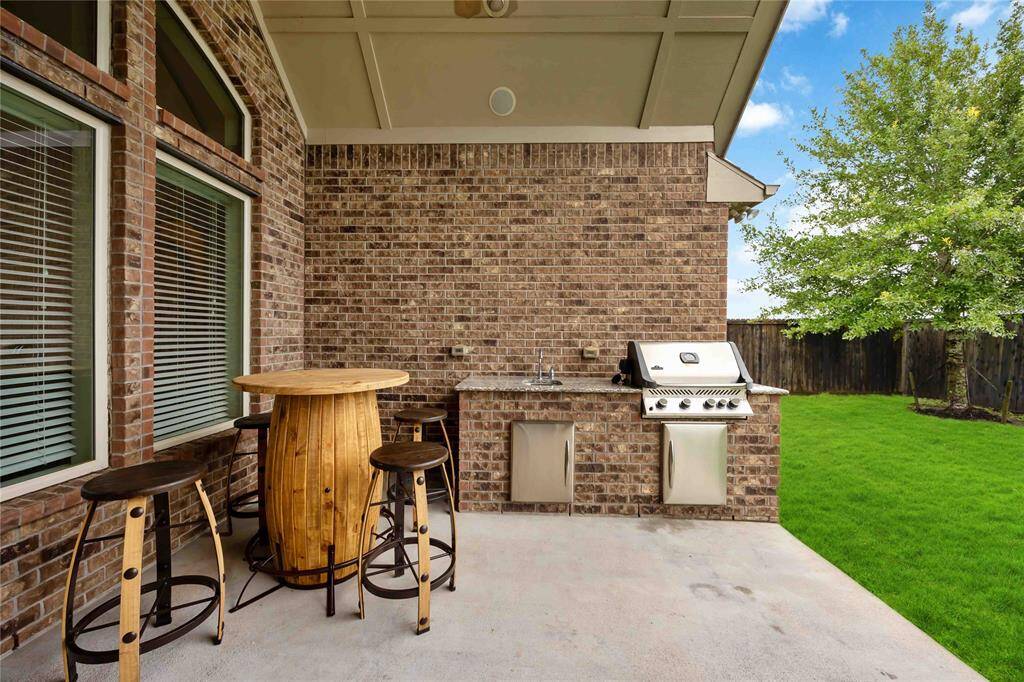 The covered patio features a built-in outdoor kitchen with a stainless steel grill, sink, and prep space—perfect for weekend grilling and any occassions.
