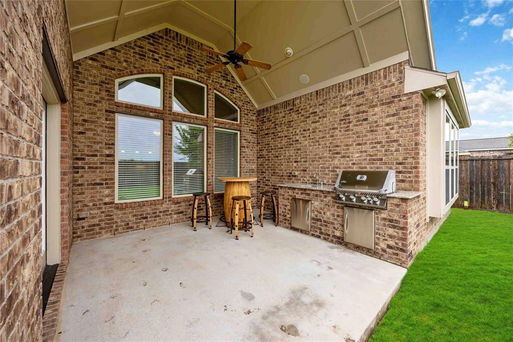 Step into a spacious covered patio featuring a vaulted ceiling, ceiling fan, and warm brick detailing