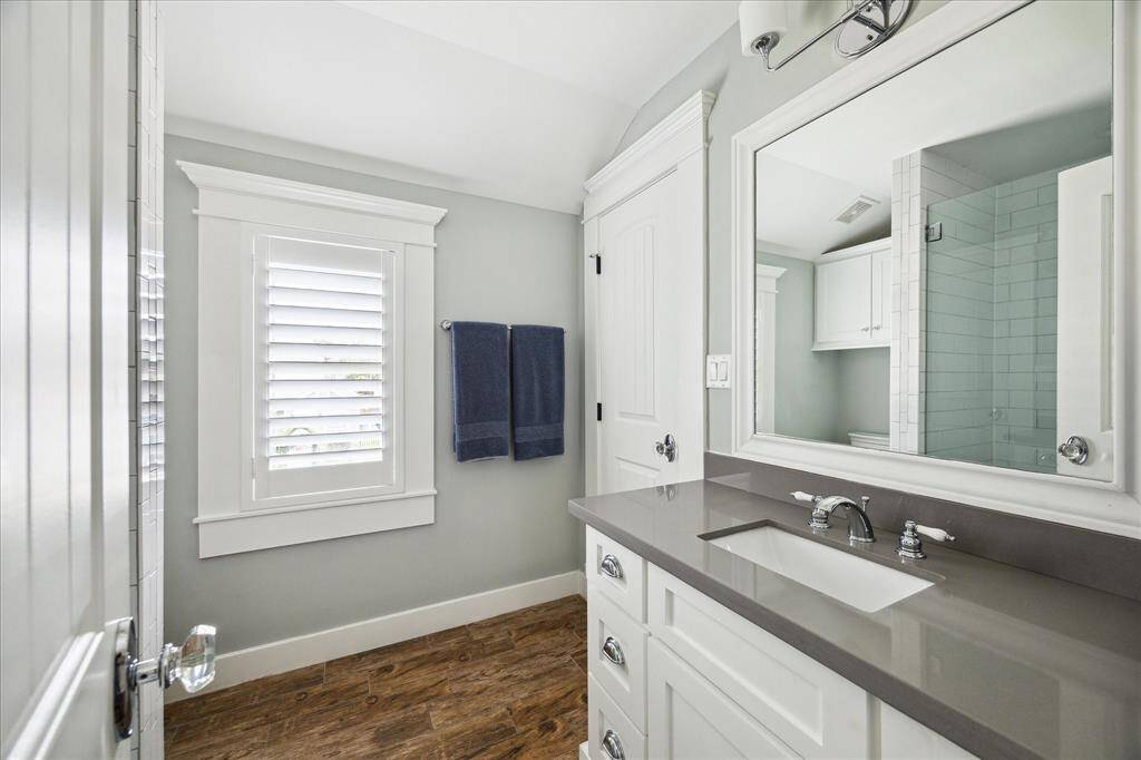 Conveniently designed for flexibility, this upstairs secondary bathroom is accessible from both the hallway and one of the secondary bedrooms. It features a sleek quartz countertop, classic cabinetry, and wood-look tile flooring for added warmth and durability. A large glass-fronted, tiled walk-in shower adds a modern and functional touch.