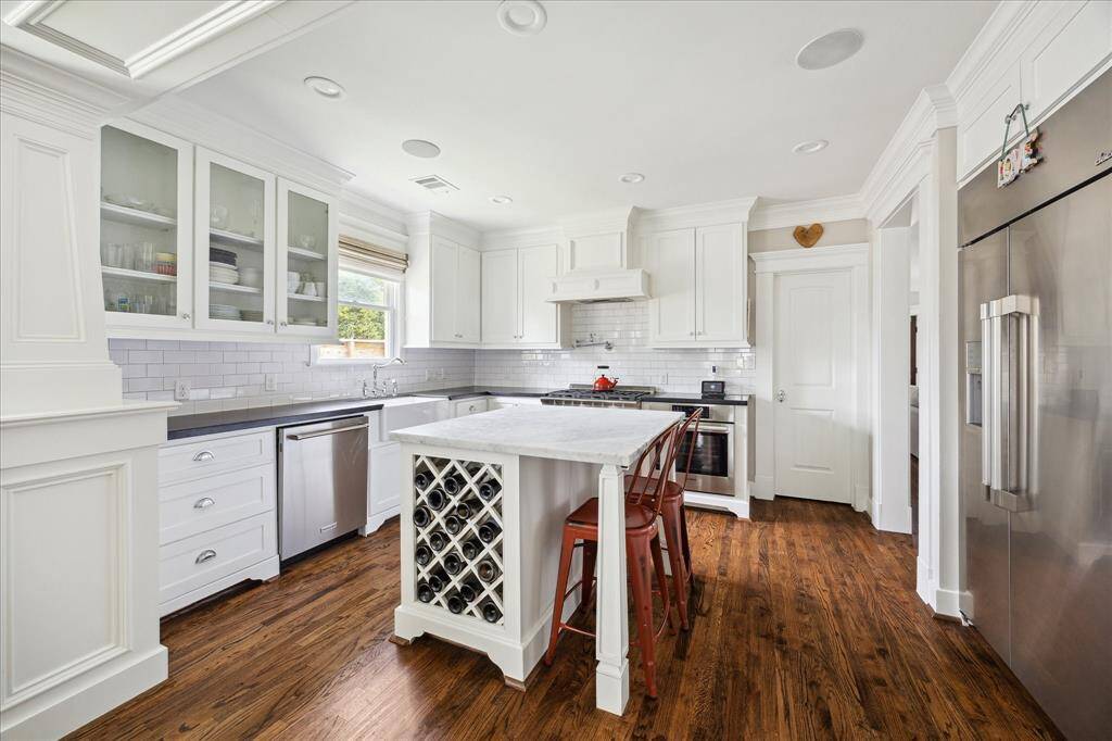 Thoughtfully designed and beautifully finished, this kitchen features classic white cabinetry, a subway tile backsplash, and sleek stone countertops. Glass-front upper cabinets add a touch of elegance, while recessed lighting and a large window provide a bright, inviting atmosphere. The layout offers ample workspace and seamless flow for everyday cooking or entertaining.