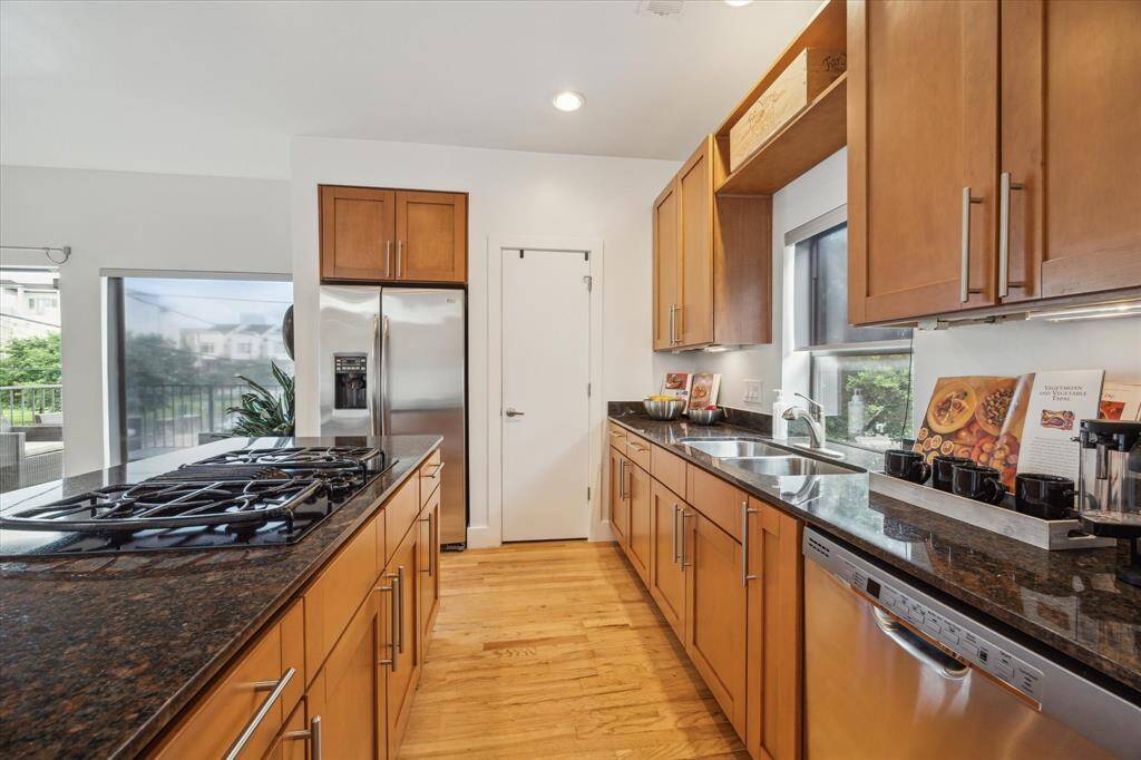 Modern kitchen with stainless steel appliances, maple cabinets, and a central island with bar seating. Bright and open layout with hardwood flooring and decorative accents. Ideal for cooking and entertaining.