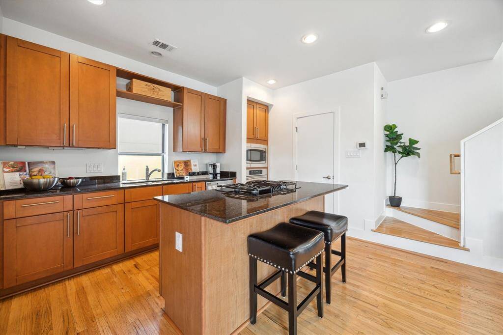 This kitchen features a central island with a granite countertop, and bar seating.   Stainless steel appliances, and an adjacent staircase.