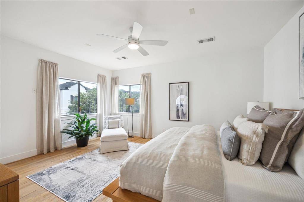 Bright and spacious primary bedroom with natural light from large windows featuring a sitting area,  ceiling fan, and hardwood floors.