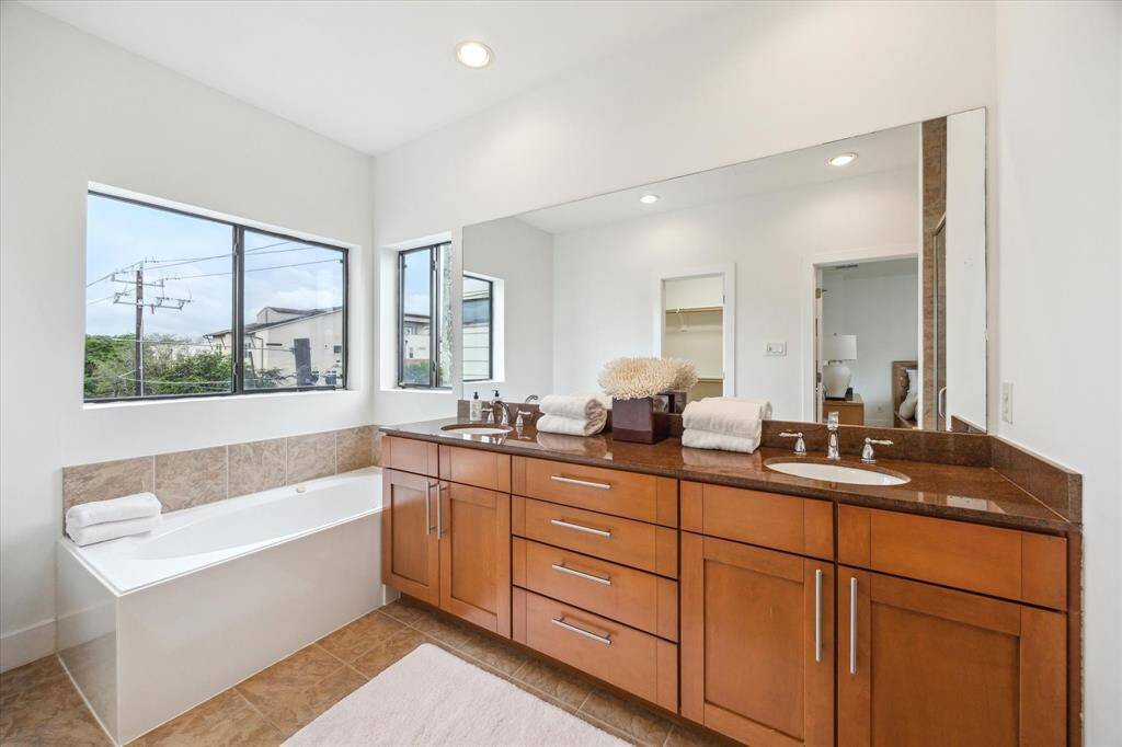 The primary bathroom features a spacious design with a large mirror, dual sinks, and ample cabinet storage. It includes a bathtub set beneath a window providing natural light.