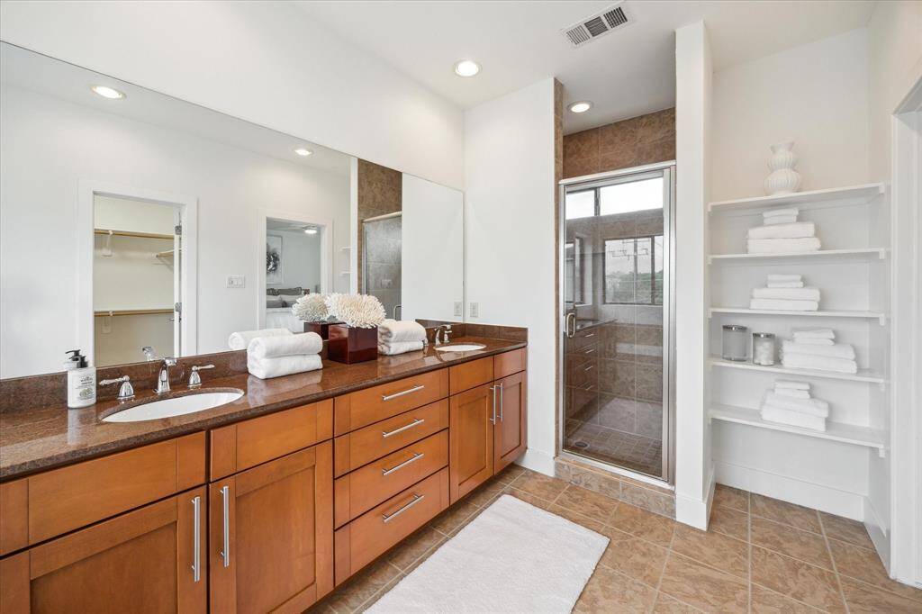 This spacious bathroom features a double vanity and includes a glass-enclosed shower and open shelving for storage.