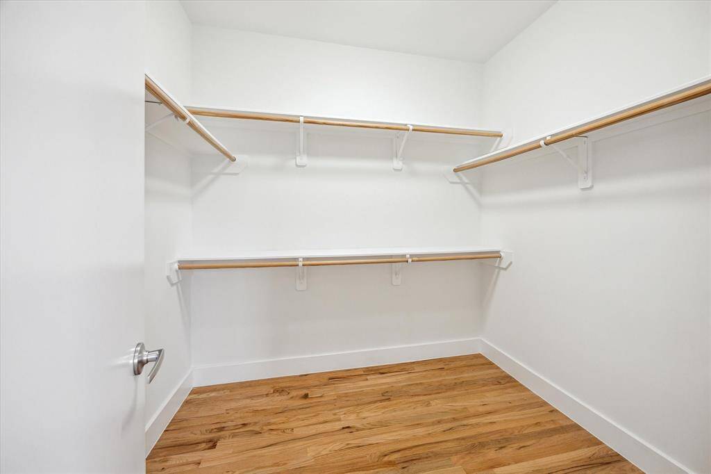 The spacious walk-in closet features white walls, multiple wooden shelves for ample storage, and a hardwood floor, offering a clean and organized space.
