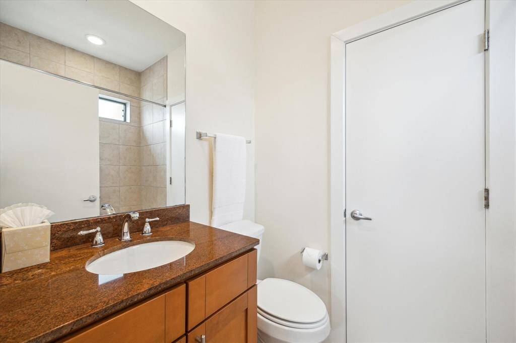 This bathroom features a sleek design with a modern brown granite countertop, under-mount sink, and polished fixtures. It includes a large mirror, a shower with tiled walls.