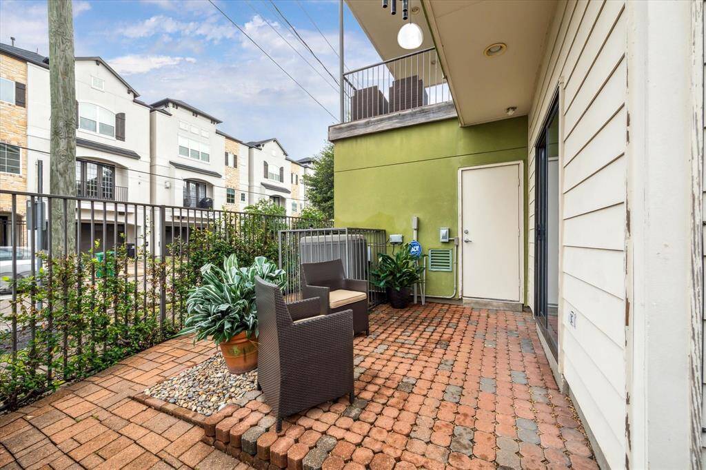 Charming patio with brick flooring and space for cozy seating.  It features a fenced area and overlooks a view of neighboring townhouses. Ideal for outdoor relaxation.