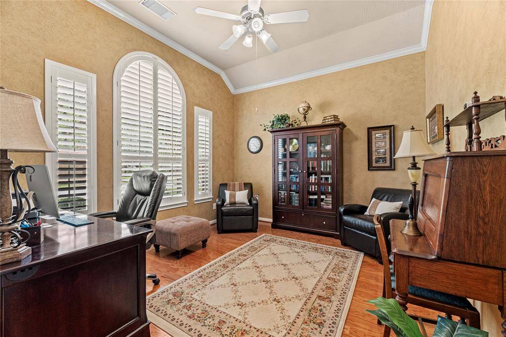 The home office offers a warm and refined atmosphere with rich wood flooring, bright windows adorned with classic shutters, and elegant crown molding adding a touch of sophistication.