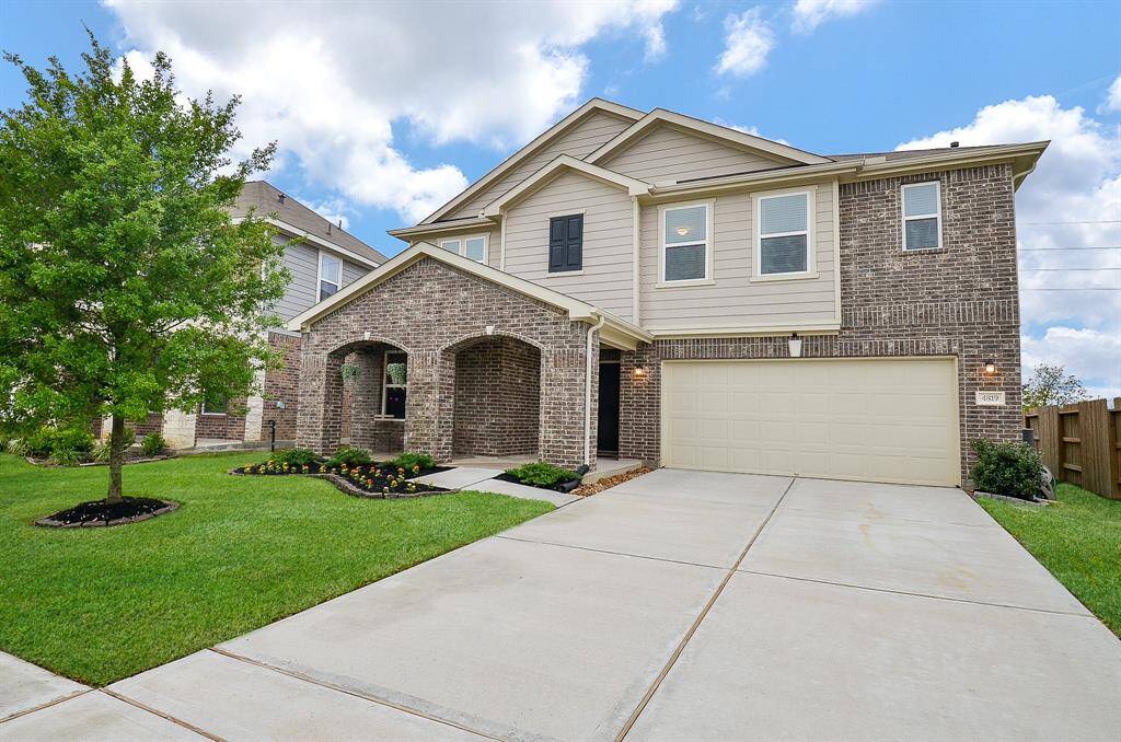 This is a modern two-story home with a brick and siding exterior. It features a large driveway leading to a two-car garage and a well-maintained front yard with a tree and landscaping.