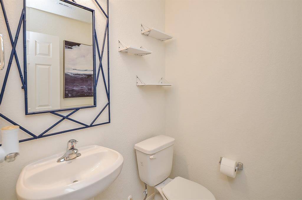 This is a compact, modern half bathroom featuring a minimalist design. It includes a wall-mounted sink, a toilet, and a stylish mirror with a geometric frame. There are small shelves for storage and a neutral color palette that enhances the sense of space.
