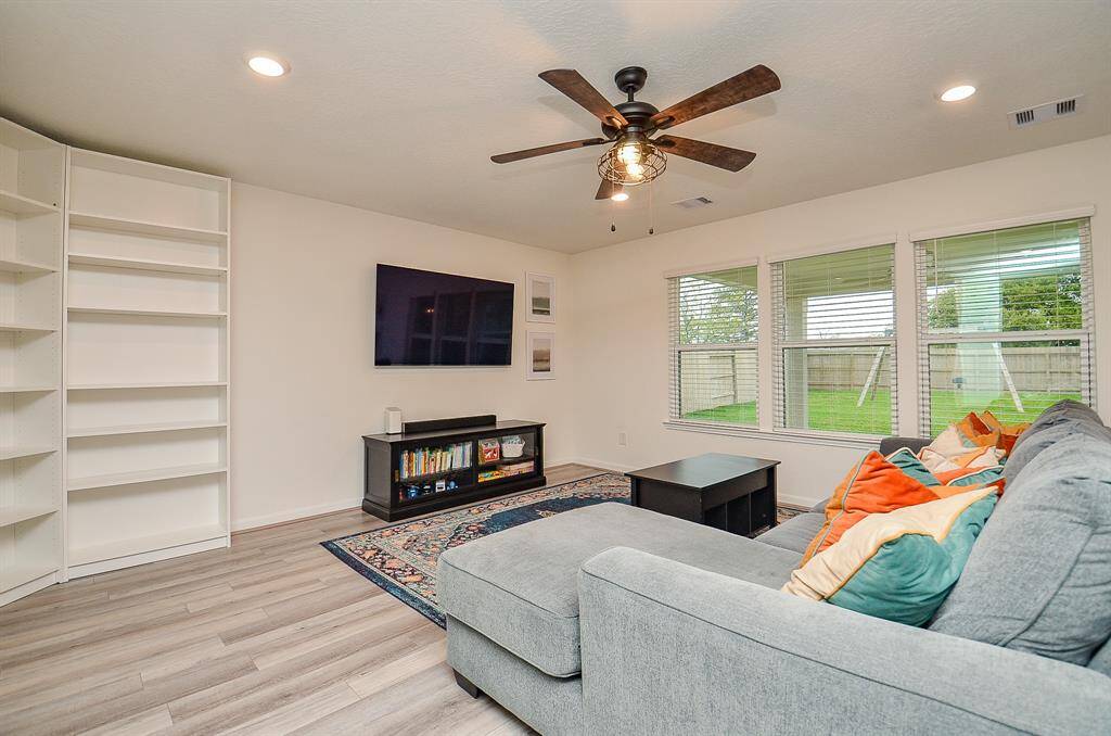 This cozy living room features a large area, it has a ceiling fan, recessed lighting, and large windows offering plenty of natural light with views of the backyard. The space is warm and inviting, ideal for relaxing or entertaining.
