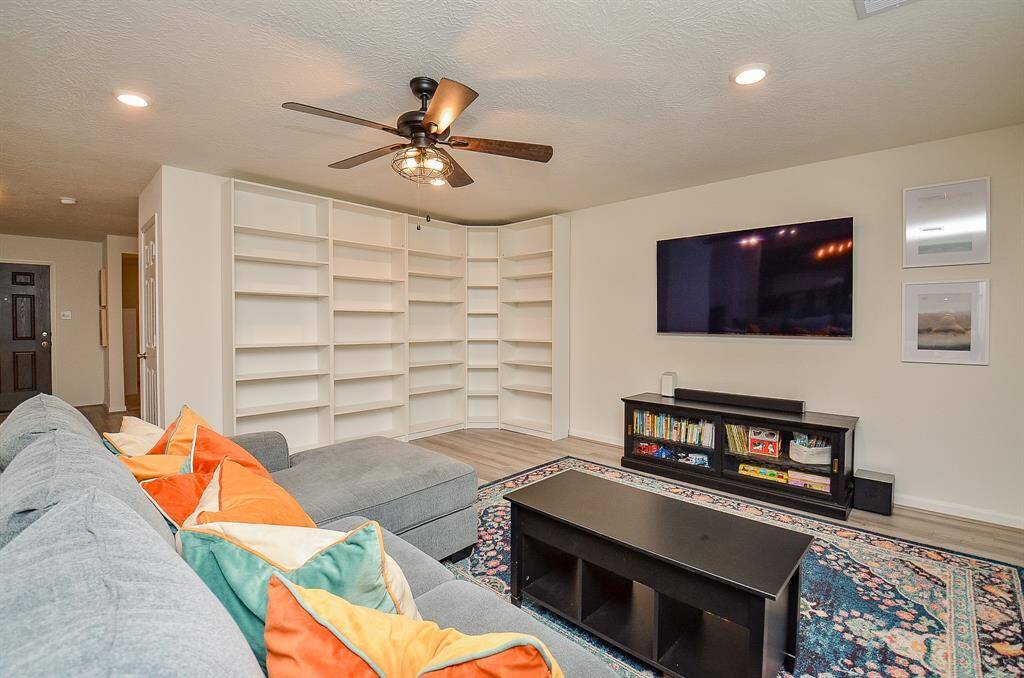This inviting living room features a spacious room is well-lit with recessed lighting and a ceiling fan, complemented by a cozy area rug.