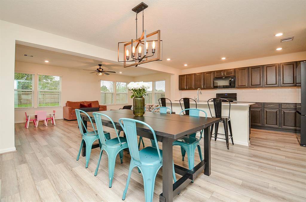 This open-concept living and dining area features modern light fixtures. The neutral tones and wood lam. flooring create a warm, inviting atmosphere.