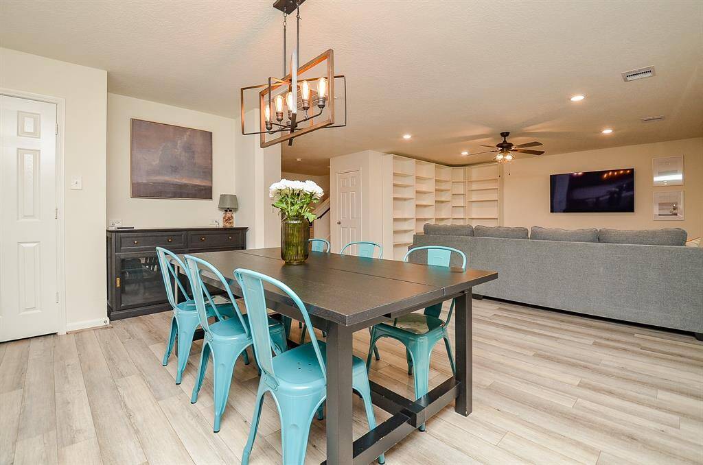 This spacious living area features an open layout with modern lam. wood flooring, a cozy seating area, and a dining space with a stylish light fixture. Large windows provide ample natural light, and built-in shelves offer plenty of storage.