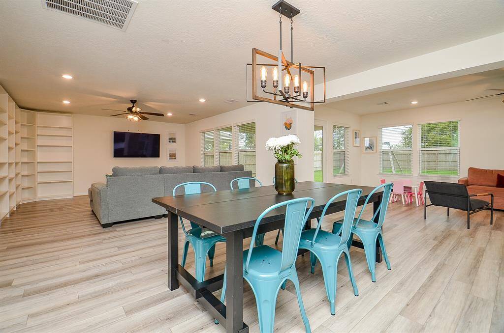 This open-concept space features a spacious dining area with a modern light fixture. The room flows into a bright living area with large windows and a ceiling fan. The kitchen has dark wood cabinetry, providing a sleek contrast to the light wood flooring.