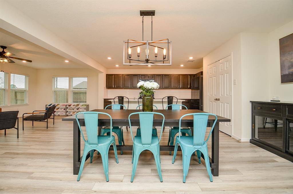 This modern kitchen features dark wood cabinets,  appliances, and a sleek, light wood floor. The space includes a central island with a undermount sink and ample countertop space, complemented by under-cabinet lighting and a contemporary backsplash. Perfect for cooking and entertaining.