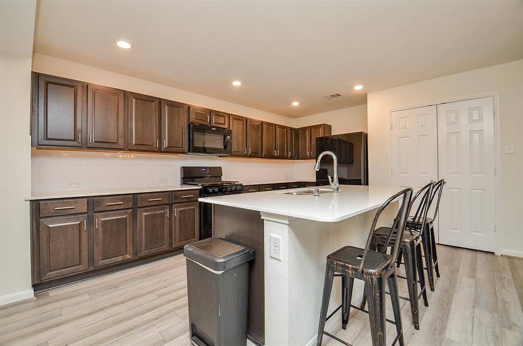 This photo showcases a spacious, open-concept living area, sunroom with a modern kitchen. It features a large island with a sink, a dining area with a stylish light fixture, and a cozy living room with plentiful natural light from multiple windows. The space has contemporary flooring and ceiling fans for comfort.