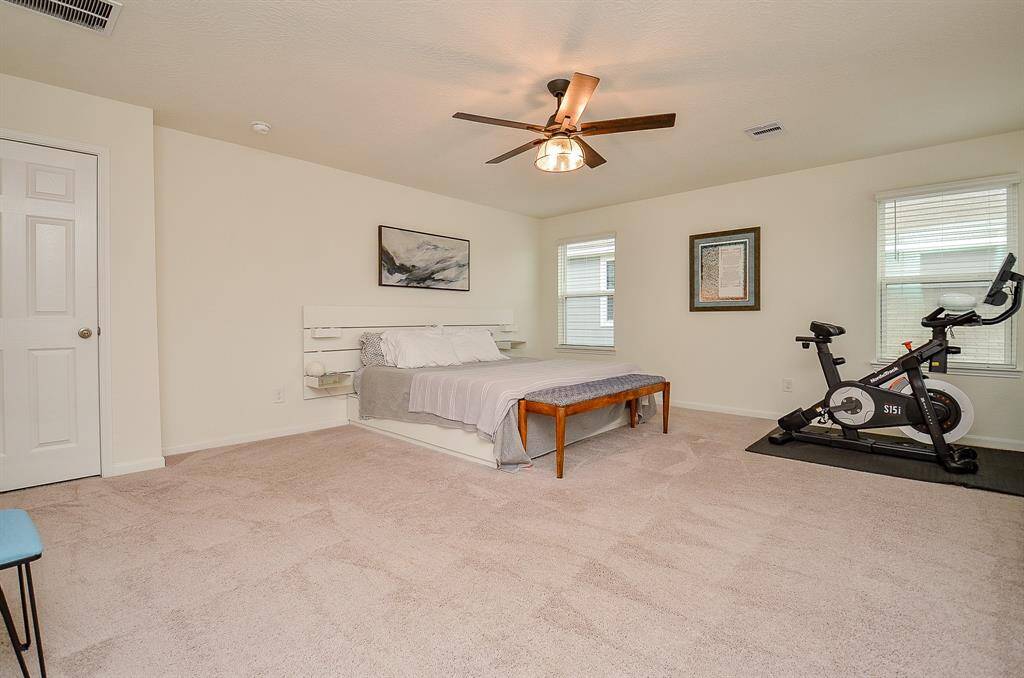 This is a cozy children's bedroom featuring a playful, themed bedspread, light-colored walls, and carpeted flooring. It has two windows with curtains, a small nightstand, and cheerful wall art, creating a bright and inviting atmosphere.