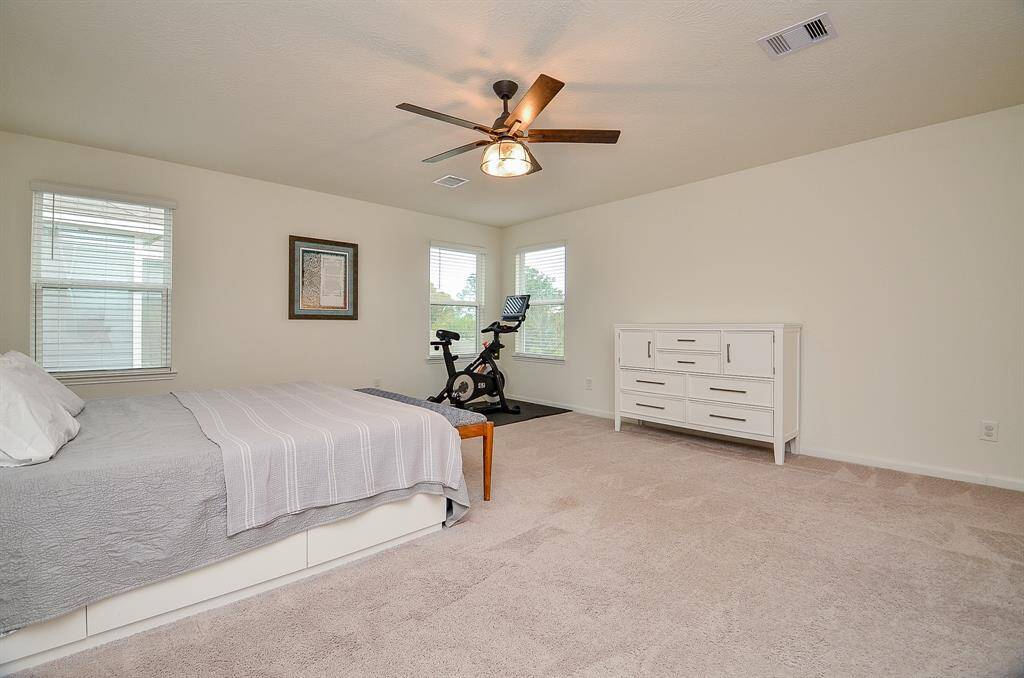 This photo shows a spacious laundry room with a modern washer and dryer set. The room features light-colored walls, tile flooring, and a long shelf above for additional storage.