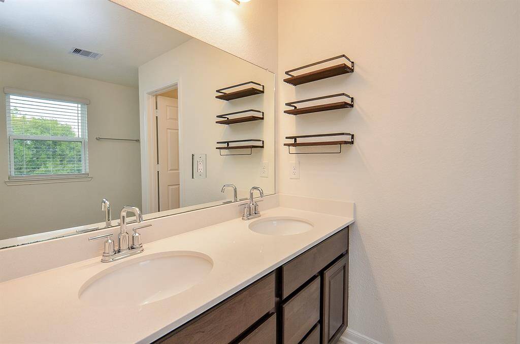 This bathroom features a sleek, modern vanity with a large mirror and ample cabinet storage. The neutral tile flooring complements the light wall color, creating a bright and inviting space.