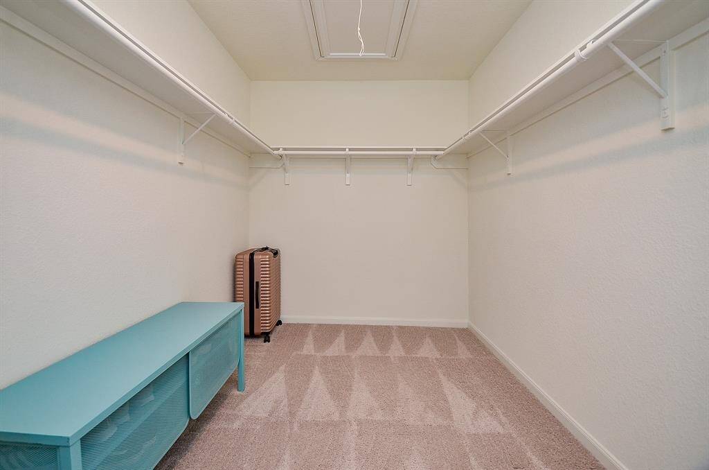 Spacious bedroom with neutral tones, featuring a ceiling fan,  enough space for an exercise bike, and ample natural light from two windows. Includes a comfortable bed with a bench at the foot and tasteful wall art.