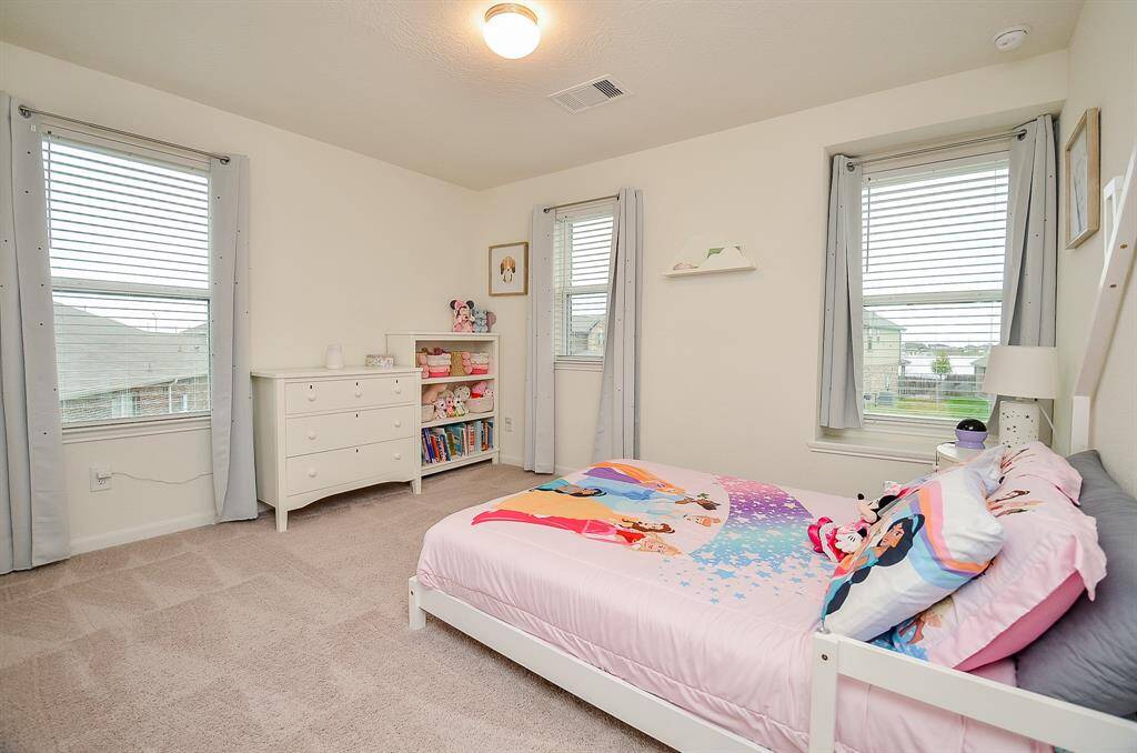 This photo features a spacious walk-in master closet with carpeted flooring, dual-level shelving, and a ceiling hatch.
