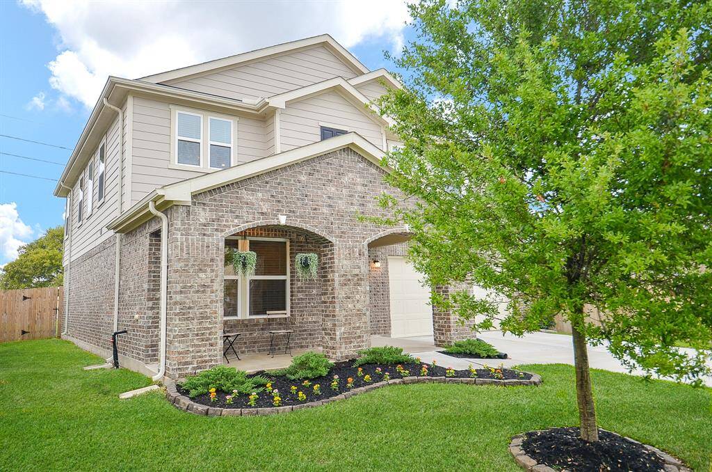 Charming two-story brick home with a welcoming archway entrance. The front yard features a well-maintained lawn, a neat flower bed, and a mature tree. Ideal for family living with a cozy porch area.