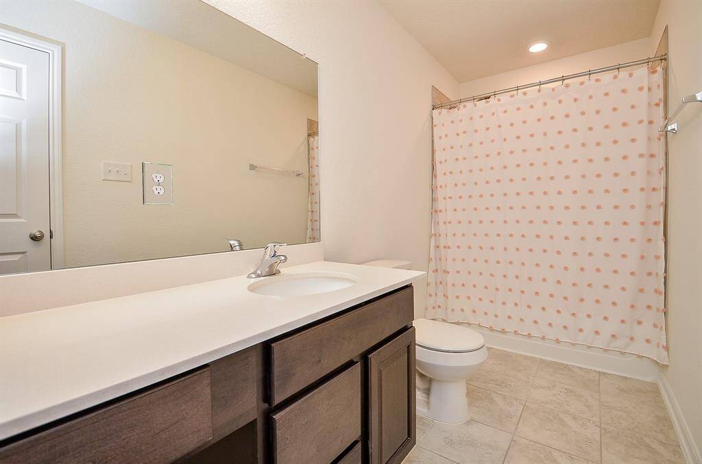 Modern bathroom featuring a sleek bathtub with a tiled shower area and dual showerheads. The room is complemented by a colorful shower curtain and a clean, neutral color scheme.