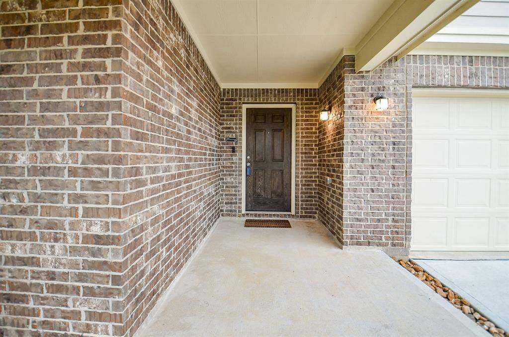 Charming brick entrance with a covered porch, featuring a dark wood like front door and two warm wall lights. Adjacent to the garage, offering a welcoming and secure entryway.
