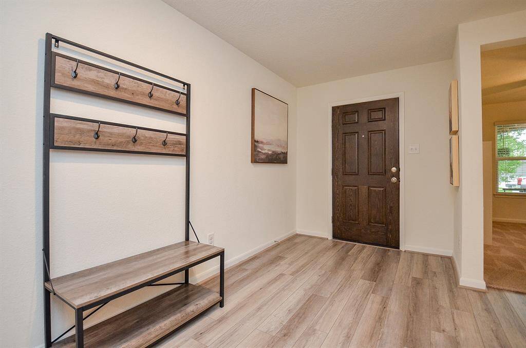 This photo showcases a welcoming entryway with light wood laminate flooring and a dark wooden like front door. There's a stylish coat rack with a bench, and the space is well-lit and open, leading into the main living area.