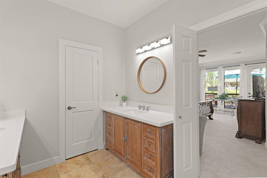 The Primary Bath sits beyond a pair of double doors. The space boasts ceramic tile flooring, lofted ceilings, and a neutral color palette.