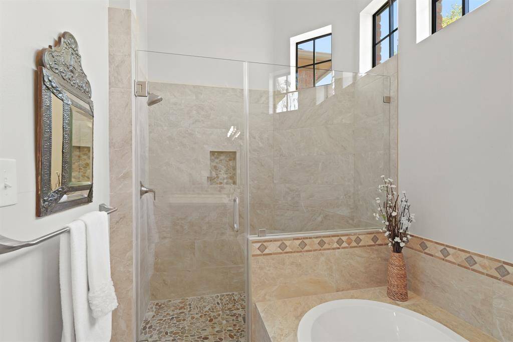 This frameless, glass shower is large in size and style. River rock tiling adds texture and charm to the niche and flooring below.